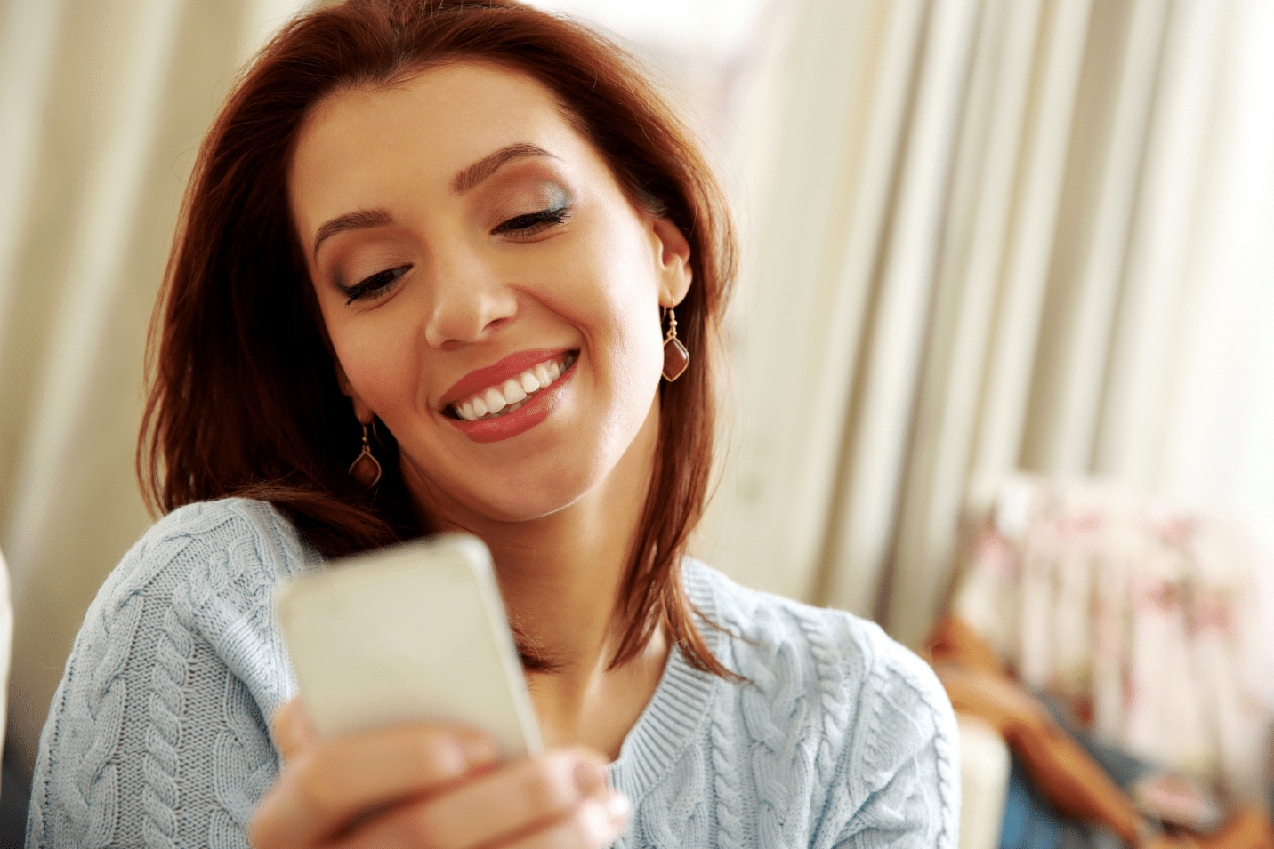 smiling-woman-holding-smartphone-at-home-SBI-300855287 1